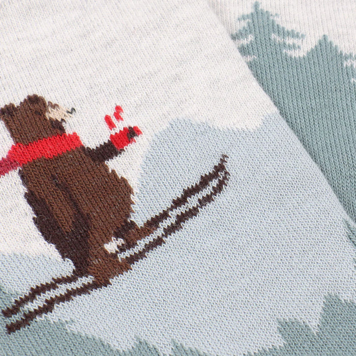 Knitted fabric with a bear design wearing a red scarf and skis on a snowy background.