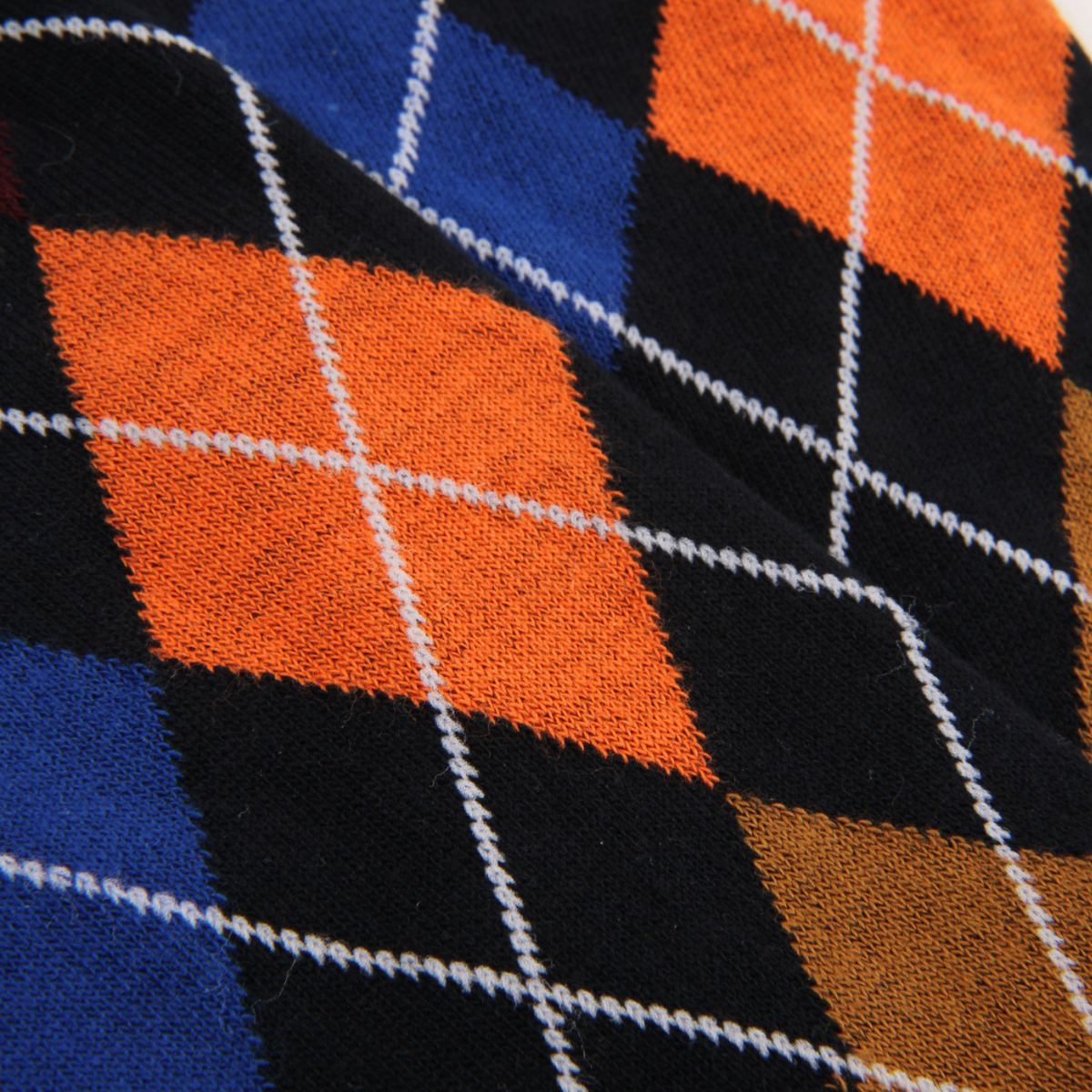 Close-up of a knitted fabric with an argyle pattern in black, bright orange, royal blue, and brown, separated by thin white lines.