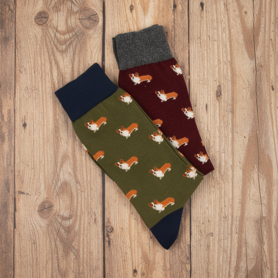 A pair of patterned crew socks laid flat on a white background. One sock is olive green with a repeating corgi print and dark navy cuffs and toes.
