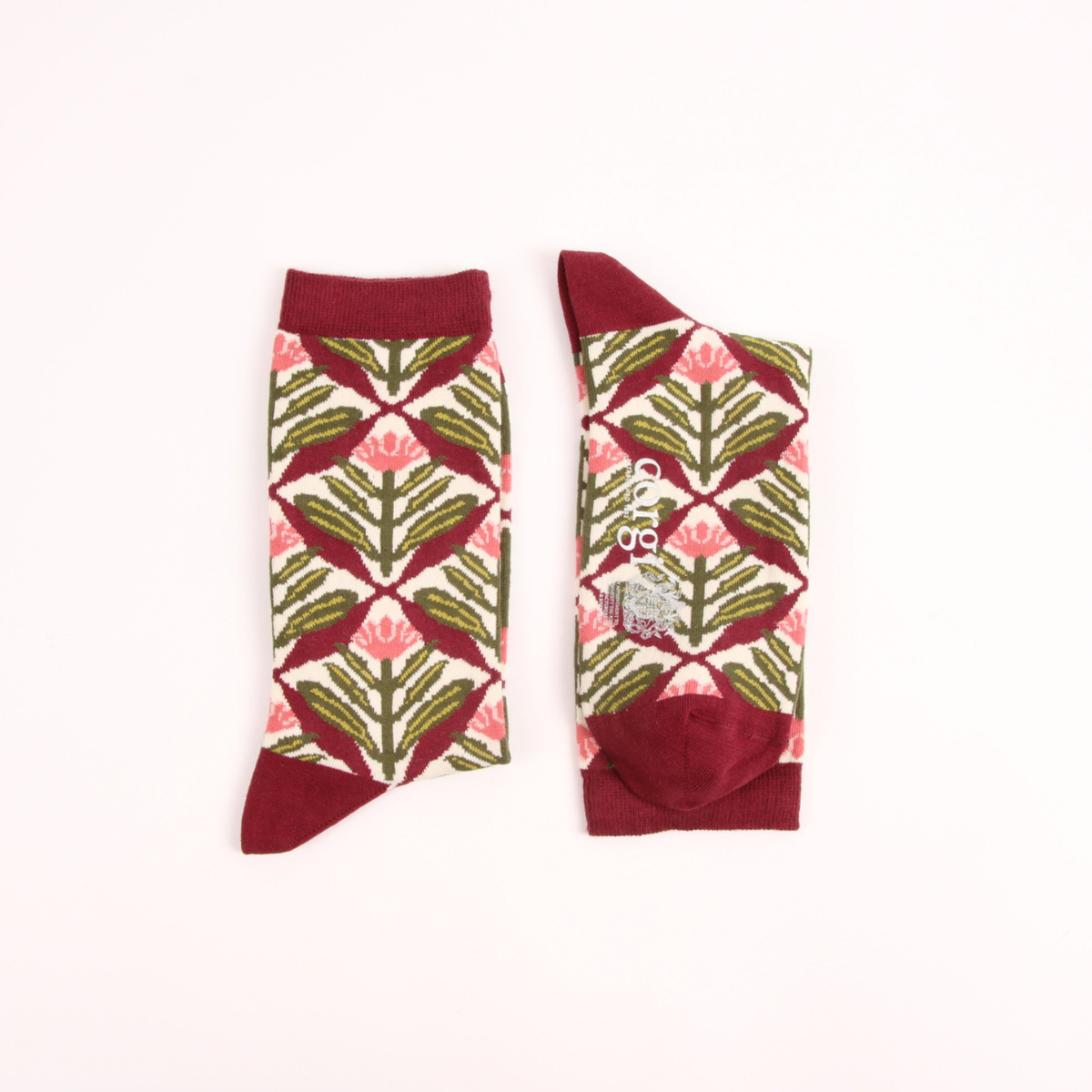 A pair of crew socks with a geometric pattern of pink lotus flowers and green leaves on a cream background, finished with solid burgundy cuffs, heels, and toes.
