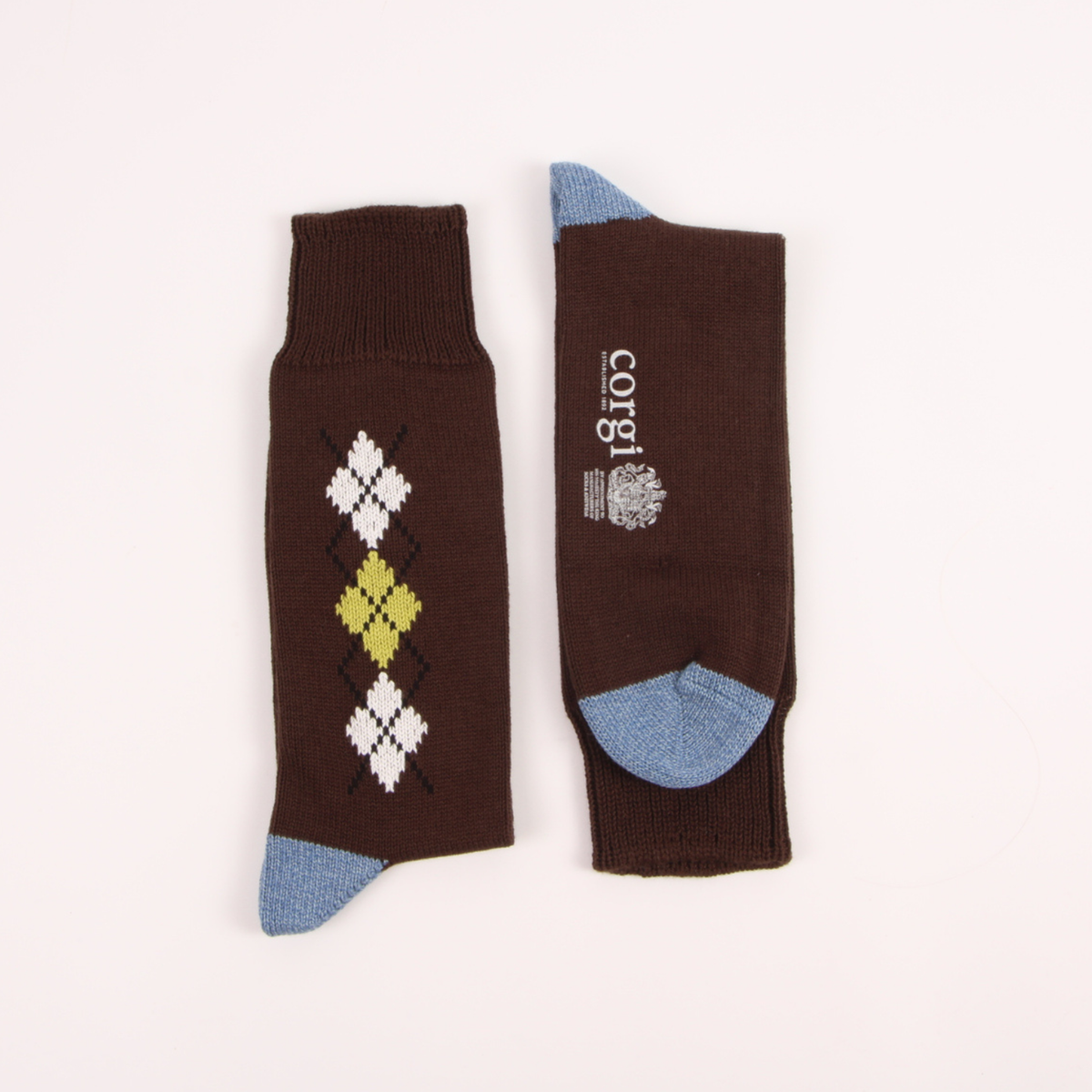 A pair of dark brown crew socks with light blue heels and toes, featuring an argyle diamond pattern in white and yellow on one sock and a white brand logo on the other, displayed on a clean white background.