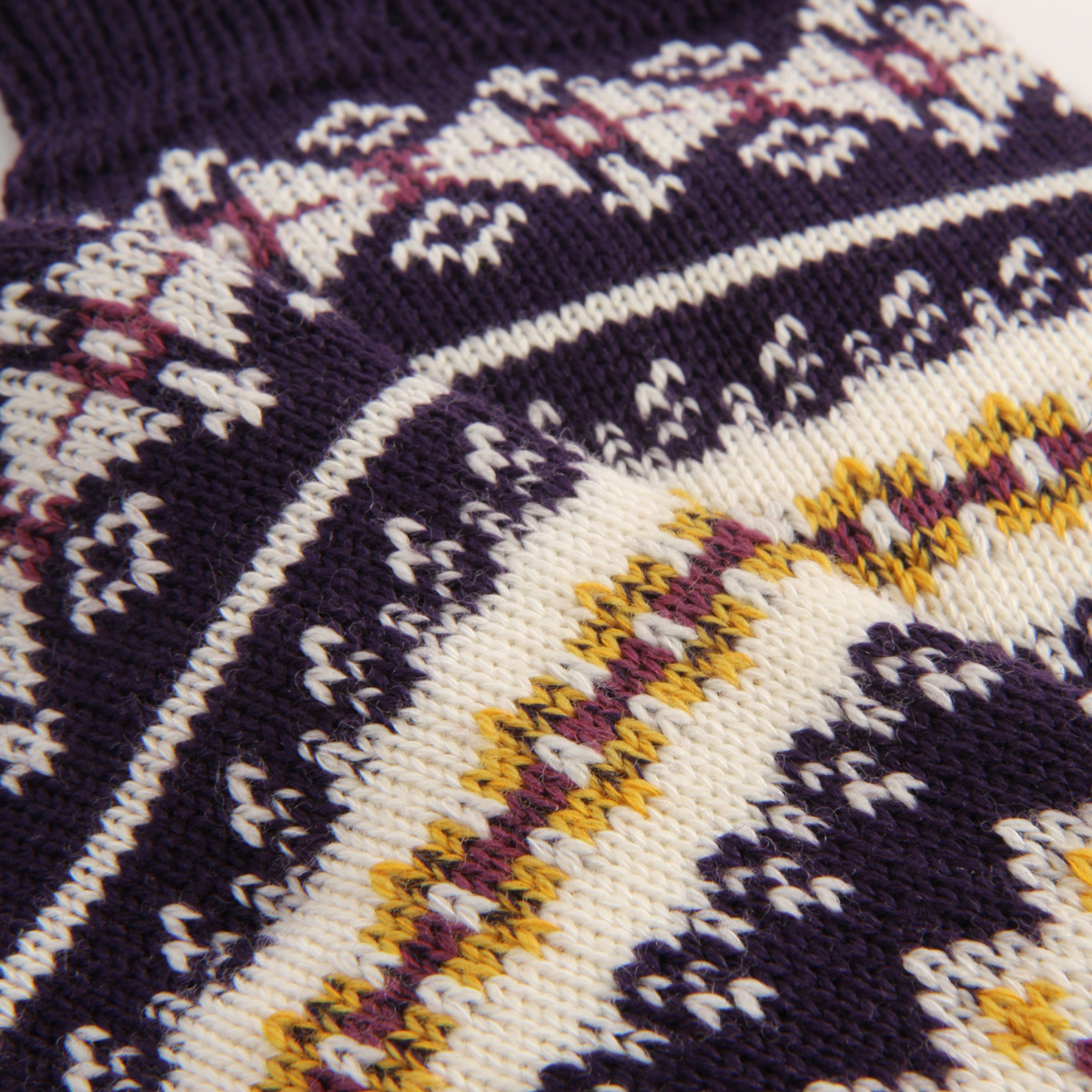 Close-up of a knitted sock showing a Fair Isle pattern in dark purple, cream, yellow, and plum.