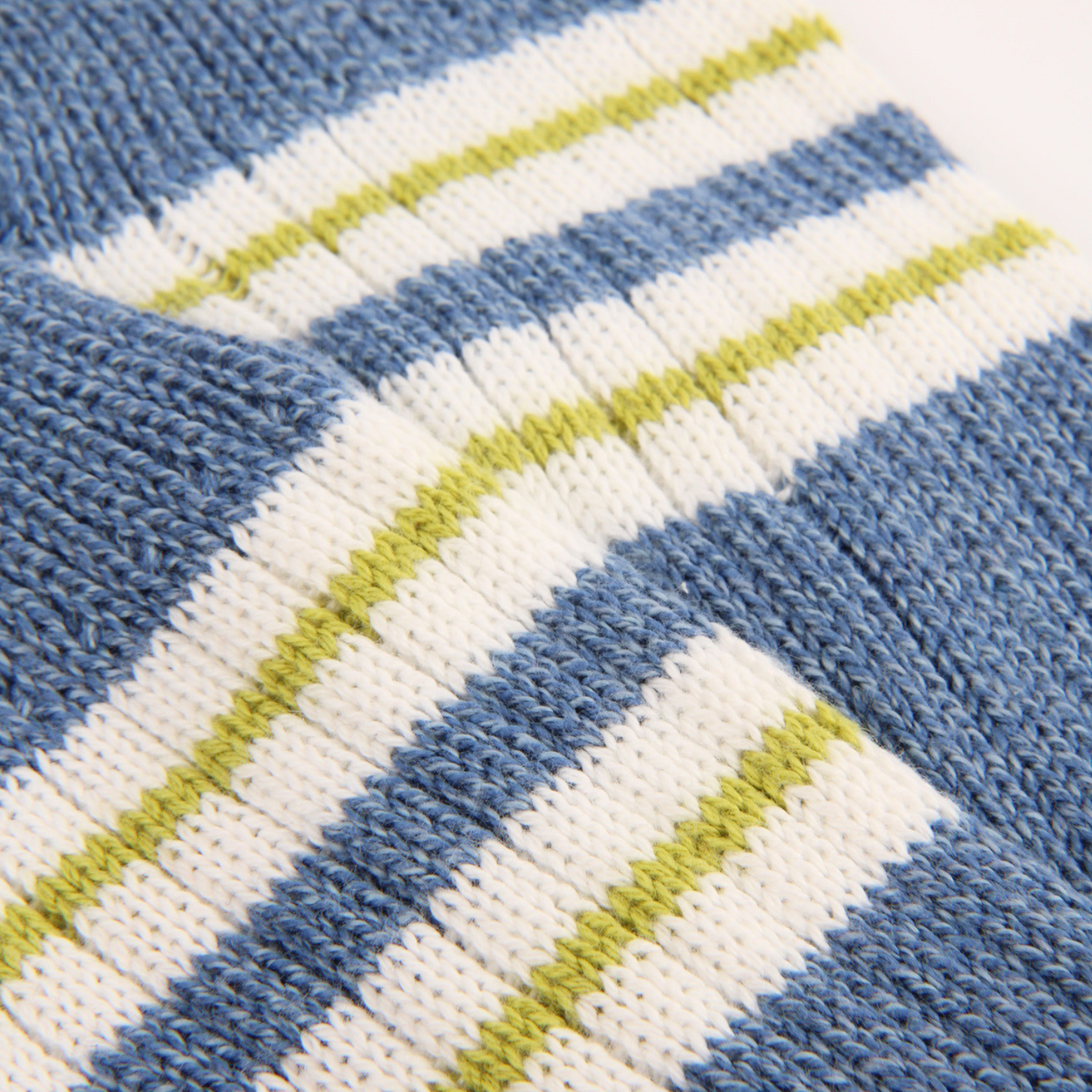 Close-up of a knitted fabric with diagonal stripes in dusty blue, off-white, and light olive green.