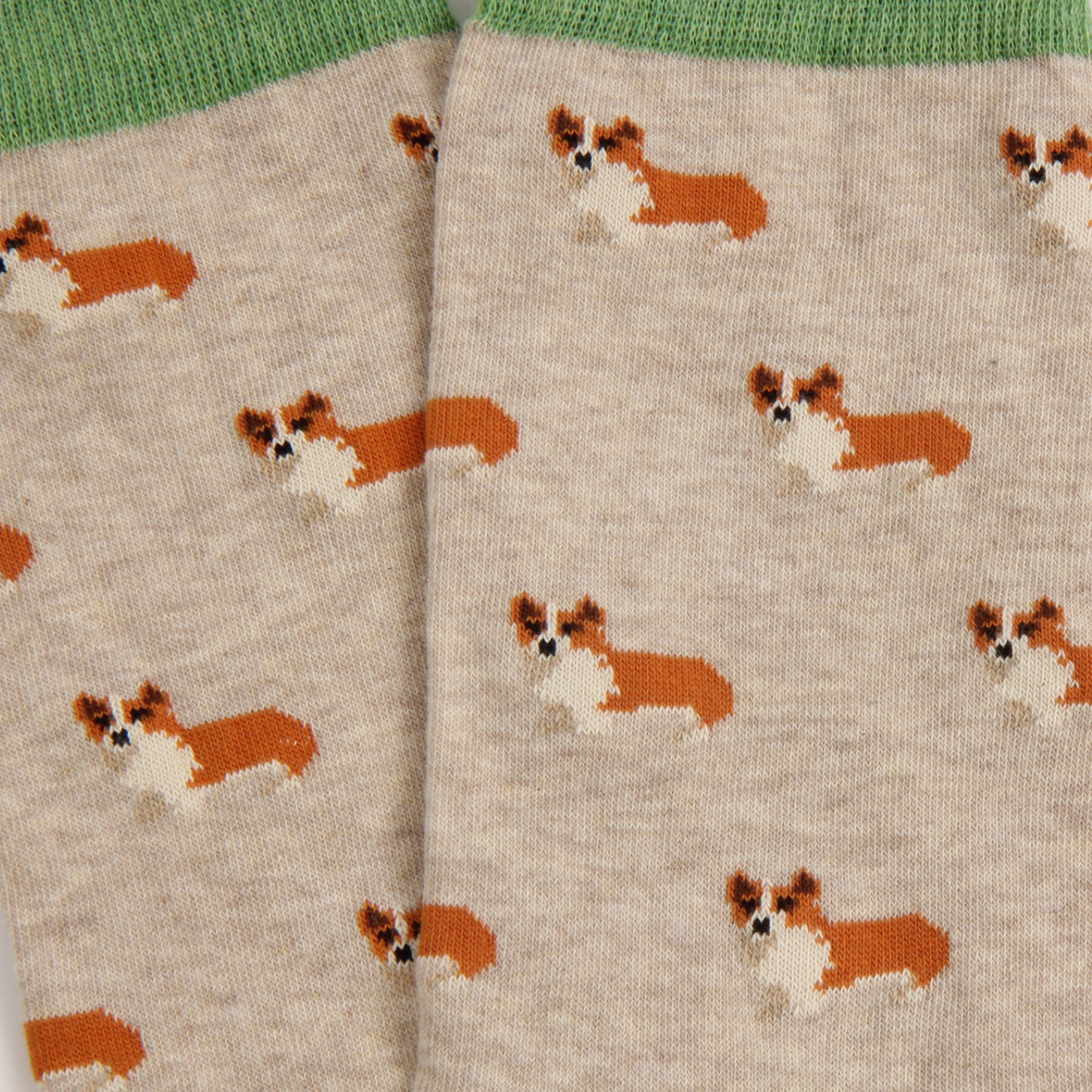 Close-up of a pair of knit socks in a light heather beige color, featuring an all-over pattern of small brown and white corgi dogs. The socks have a solid green ribbed cuff at the top.
