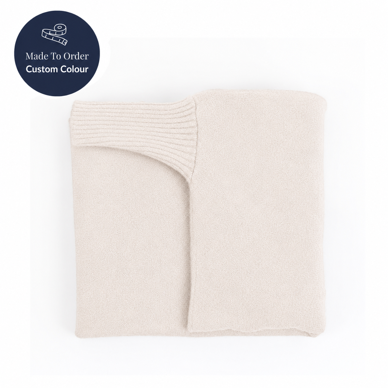 A folded cream-colored knit blanket or throw on a white background, with a dark blue circular badge in the top-left corner reading 'Made To Order Custom Colour'.