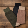 Three pairs of patterned socks in green, black, and beige on a wooden surface.