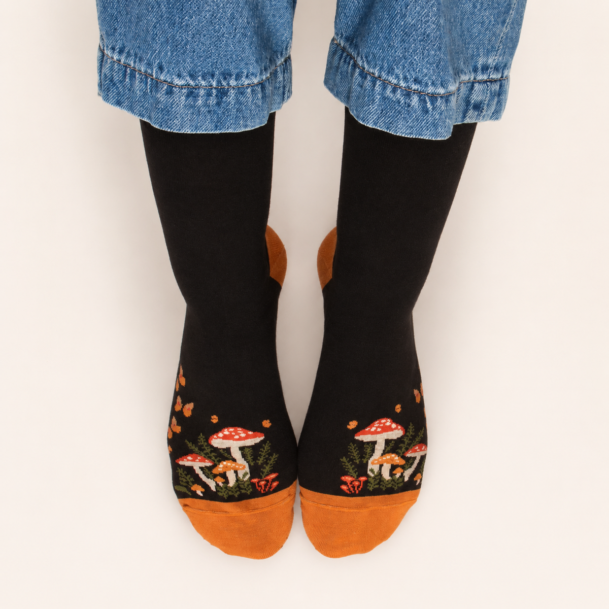 Black socks with mushroom design and orange toes worn with rolled-up jeans on a white background