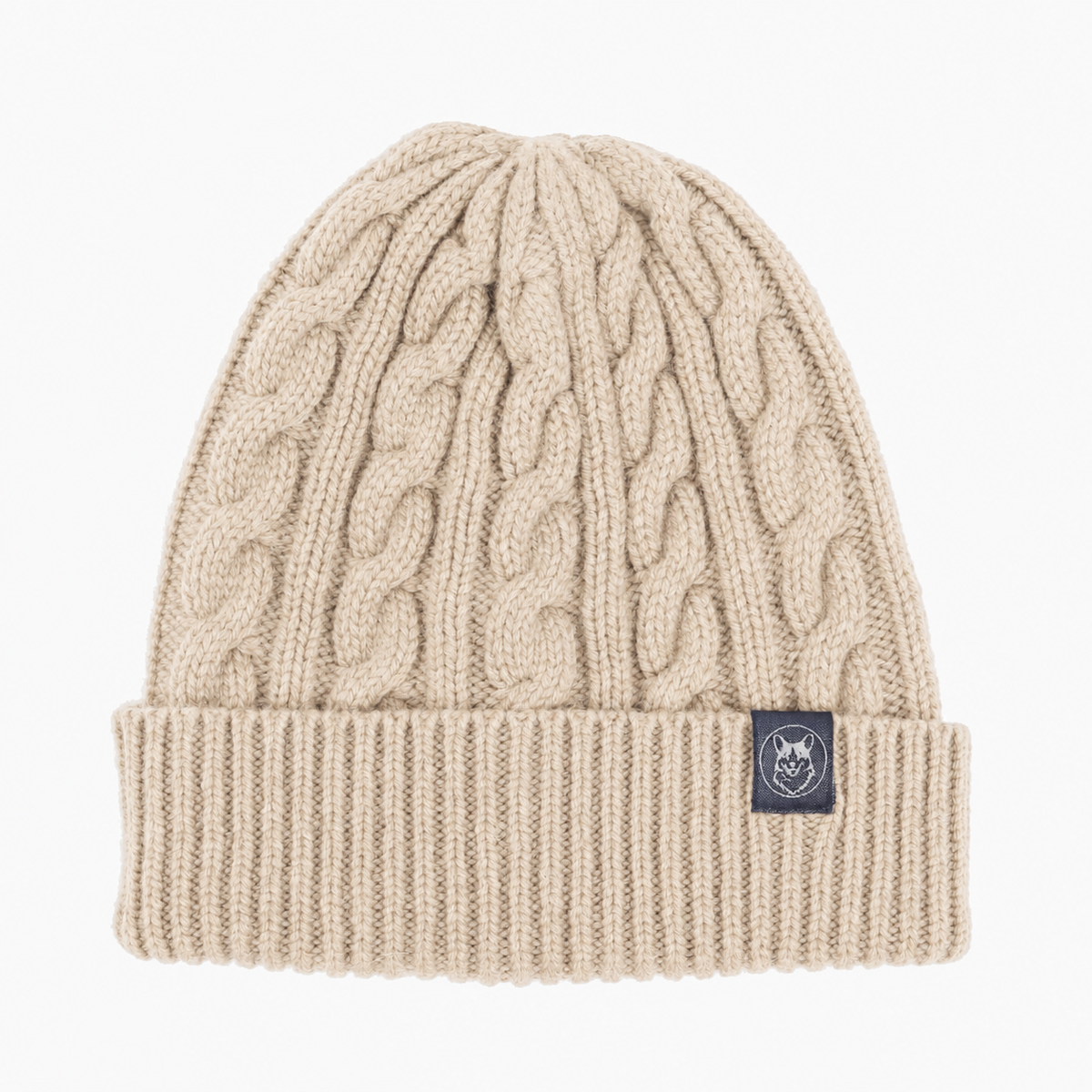 A beige cable-knit beanie hat with a ribbed cuff and a small black brand patch on the side, shown against a plain white background.