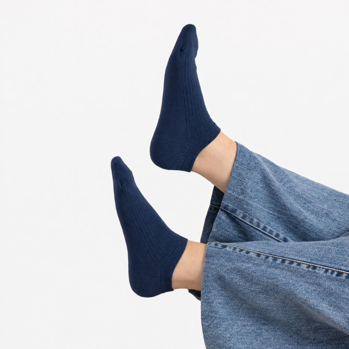 A close-up of a person's feet wearing dark navy blue ribbed ankle socks, paired with light blue wide-leg jeans, against a clean white background.