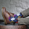 Brown leather shoes with an argyle patterned sock against a neutral background
