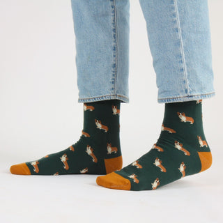 Person wearing green socks with dog pattern and blue jeans on a white background