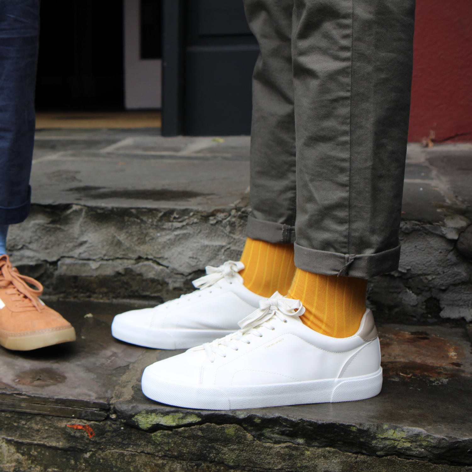 White sneakers worn with yellow socks on a stone surface