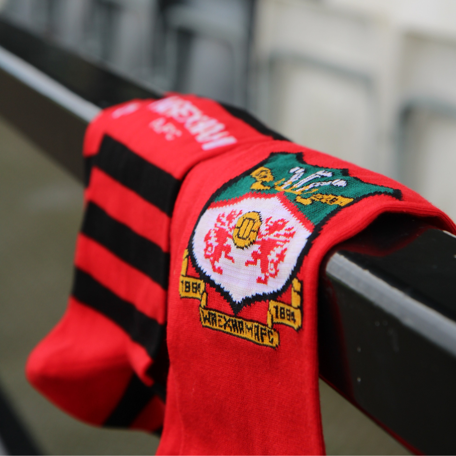 Red sports socks with black stripes and red socks with Wrexham crest  logo on a metal railing.