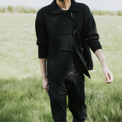 Person wearing a black coat and pants standing in a grassy field