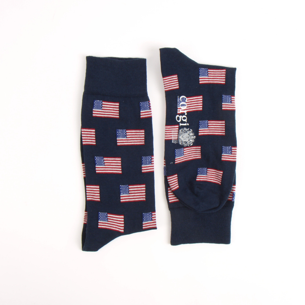 A pair of navy blue crew socks with an all-over pattern of small American flags, displayed flat on a white background. One sock shows the front pattern, and the other shows the side with a white 'corgi' brand logo.