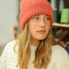 Person wearing a orange knit beanie and white sweater in an indoor setting