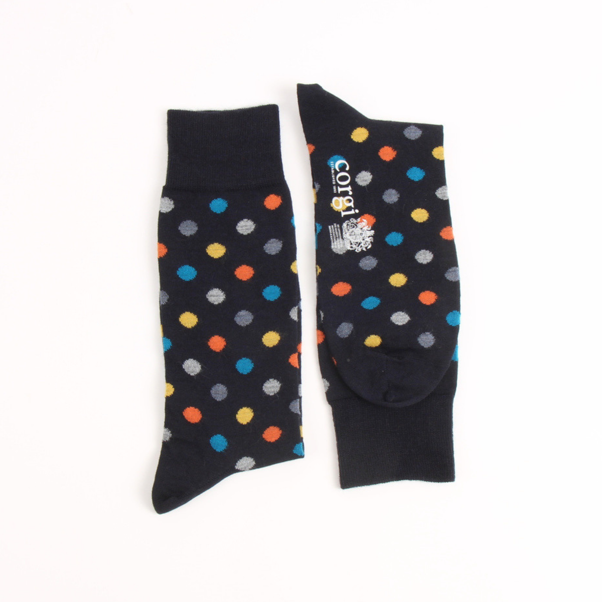 A pair of navy crew socks with colorful polka dots in blue, orange, yellow, gray, and white, displayed flat on a white background. One sock shows a white 'COTY' brand label with a small graphic.