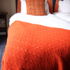 Close-up of an orange textured blanket on a bed with white bedding.