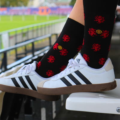 Person wearing black socks with red patterns and white Adidas sneakers on a stadium bench.