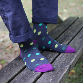 Person wearing dark blue socks with colorful polka dots sitting on a wooden bench.
