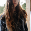 Person with long wavy hair wearing a dark patterned sweater.