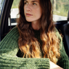 Woman with long brown hair wearing a green sweater sitting inside a vehicle.
