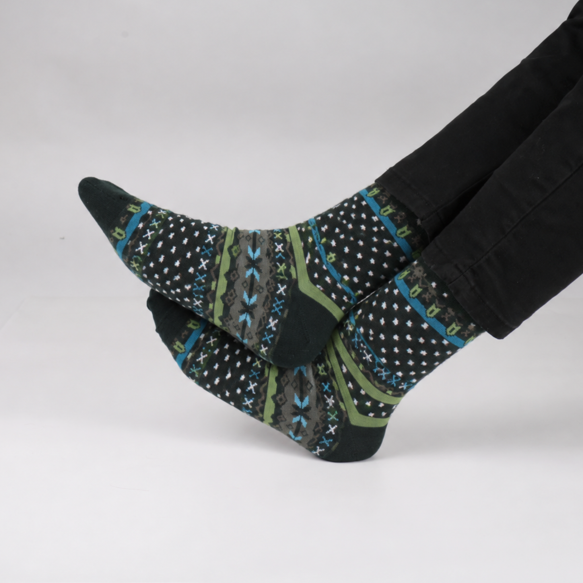 A pair of patterned crew socks worn on feet with black pants, photographed against a clean light gray studio background.