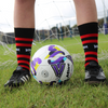 Person wearing black and red striped socks with a soccer ball on a grass field.