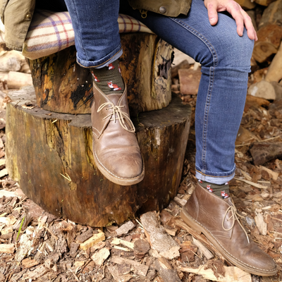Person wearing brown boots and blue jeans sitting on a wooden log in a forest setting.