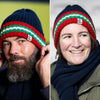 Two people wearing knit hats with red, green, and white stripes, one with a beard and the other smiling.