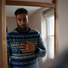 A man wearing a colorful Fair Isle sweater with geometric patterns, looking at himself in the mirror.