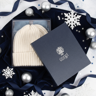 White knit beanie and blue fair isle socks inside a branded navy box on a white background