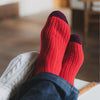 A pair of red cashmere socks with a ribbed design and contrasting wine colour toe, worn on feet.