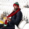 A man wearing the Red Wall scarf and hat in the football stadium stands.