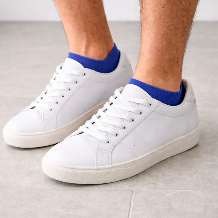 White sneakers worn with blue socks on a light gray floor.