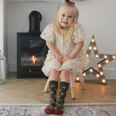 Young girl in a floral dress sitting on a stool in a room with a fireplace and decorative star.