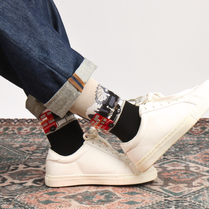 Person wearing white sneakers with a London scene socks on a patterned rug