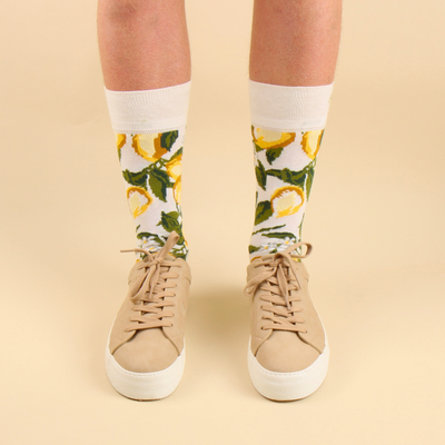 Person wearing socks with lemon pattern and beige sneakers on a beige background