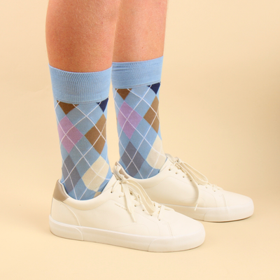 Person wearing light blue argyle socks with white sneakers on a beige background