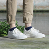 White sneakers with navy socks worn by a person standing on a wooden surface with a natural background.