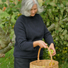Woman picking apples from a tree in an orchard wearing a roll edge British wool sweater