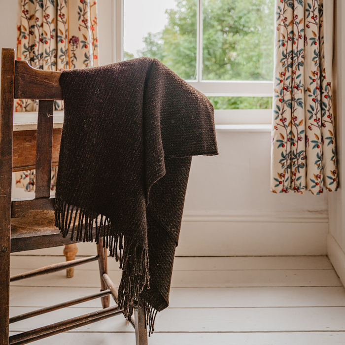Brown blanket draped over a wooden chair in a room with floral curtains and a window.