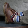 Brown leather shoe with a striped sock on a gray background