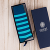 Blue and green striped sock in an open box with 'corgi' branding on a wooden surface