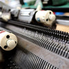 Close-up of a knitting machine with visible yarn threads and needles, illustrating the handcrafted process of making knitwear.