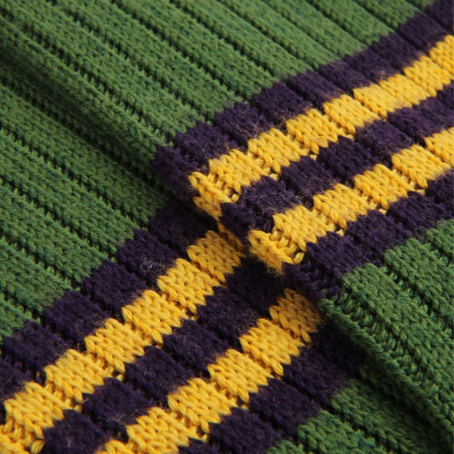 Close-up of a ribbed knit fabric with alternating green, dark purple, and yellow stripes, showing the texture and weave of the yarn.