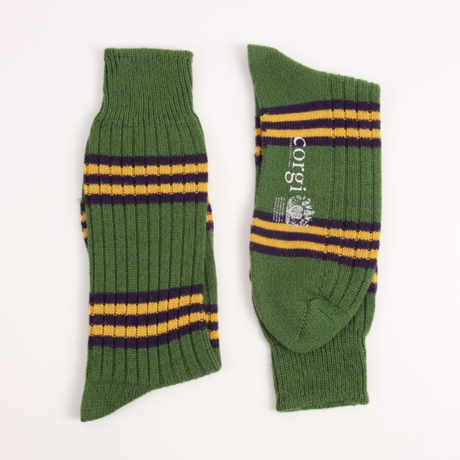 A pair of green ribbed knit crew socks with horizontal yellow and dark purple stripes, displayed flat on a white background. One sock shows the brand name 'corni' and crest logo.