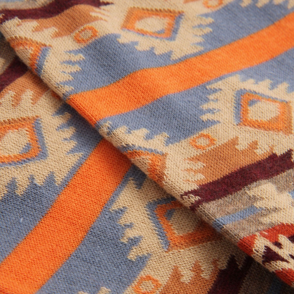 A close-up of a woven textile with a Southwestern geometric pattern in orange, dusty blue, beige, and dark red.