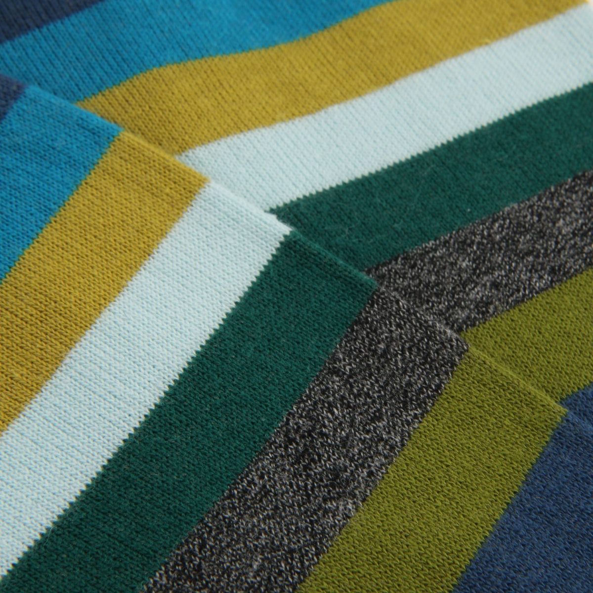 Close-up of a striped knit fabric with diagonal bands of blue, yellow, white, dark green, olive green, and heather gray.