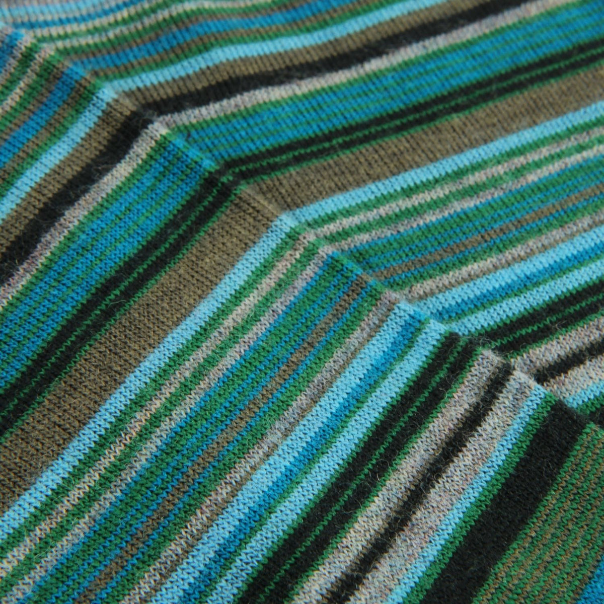 Close-up of a striped knit fabric with diagonal bands of turquoise blue, forest green, olive brown, black, and light beige.